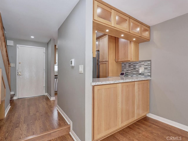 kitchen featuring wood finished floors, glass insert cabinets, tasteful backsplash, and baseboards