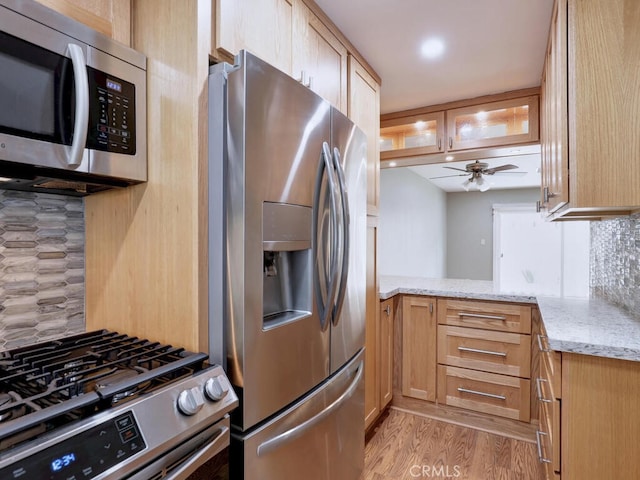 kitchen with light stone countertops, a ceiling fan, appliances with stainless steel finishes, light wood-type flooring, and backsplash