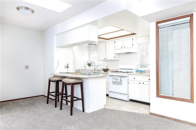 kitchen featuring a kitchen bar, white range with gas cooktop, light colored carpet, and a peninsula