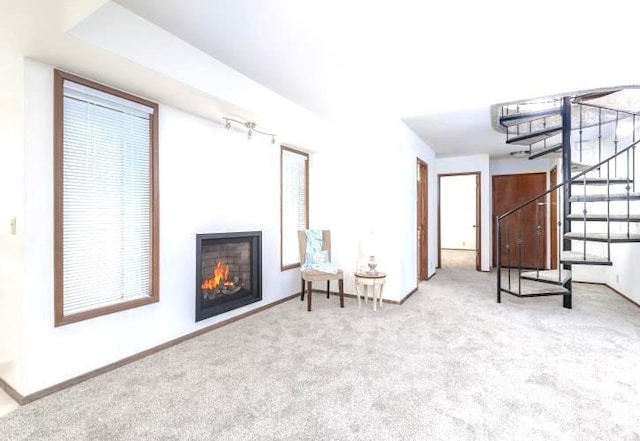 living area with carpet flooring, baseboards, a glass covered fireplace, and stairs