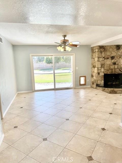 unfurnished living room featuring a stone fireplace, a ceiling fan, baseboards, and a textured ceiling