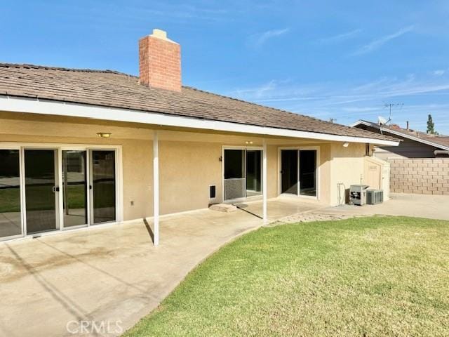 rear view of property featuring stucco siding, a lawn, a patio, fence, and a chimney