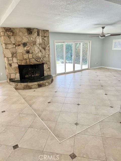 unfurnished living room featuring baseboards, a textured ceiling, a stone fireplace, and a ceiling fan