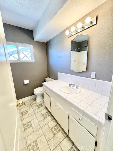 bathroom featuring toilet, stone finish floor, a textured ceiling, baseboards, and vanity