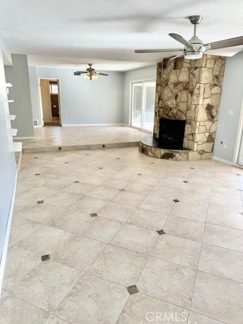 unfurnished living room with baseboards, a stone fireplace, and ceiling fan