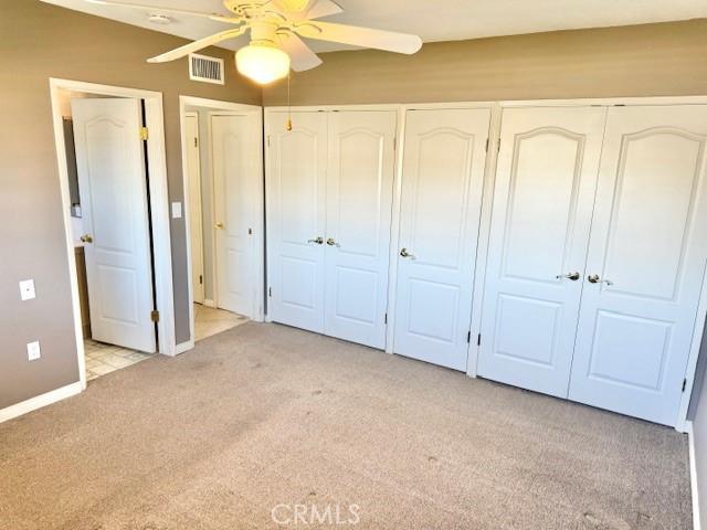 unfurnished bedroom with visible vents, light carpet, baseboards, and a ceiling fan