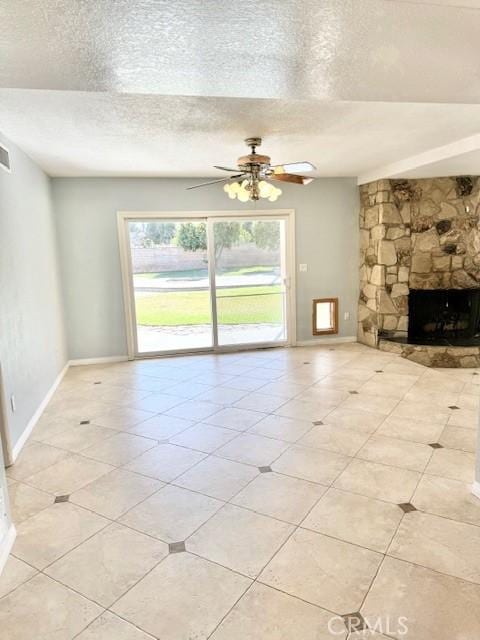 unfurnished living room with a stone fireplace, ceiling fan, a textured ceiling, and baseboards