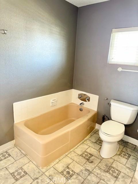 bathroom with toilet, a bath, and baseboards