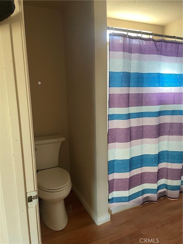 full bath featuring a shower with shower curtain, toilet, wood finished floors, and baseboards