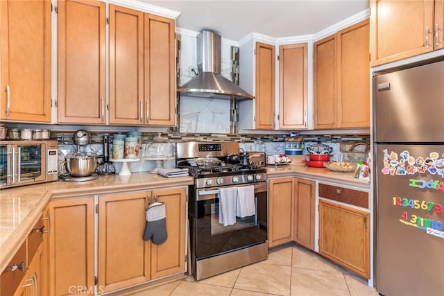 kitchen featuring tasteful backsplash, brown cabinets, appliances with stainless steel finishes, light tile patterned flooring, and wall chimney exhaust hood