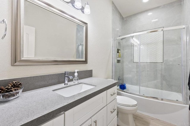 full bath with enclosed tub / shower combo, toilet, wood finished floors, and vanity