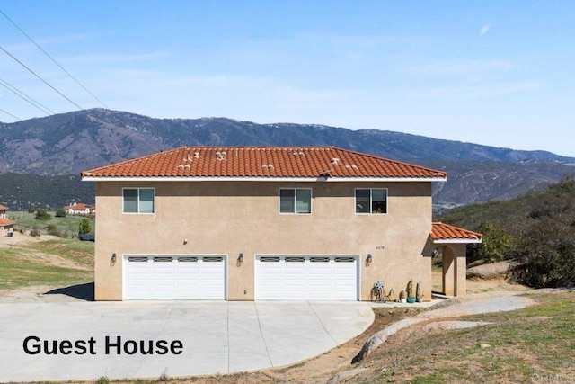 view of side of home featuring a mountain view, an attached garage, stucco siding, and a tile roof