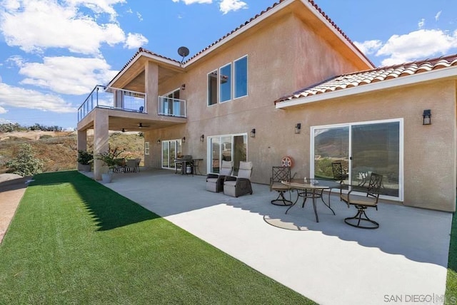 back of property with a patio, a balcony, a yard, and stucco siding