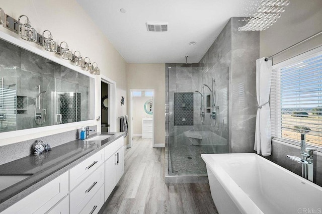 bathroom featuring visible vents, double vanity, a stall shower, wood finished floors, and a sink