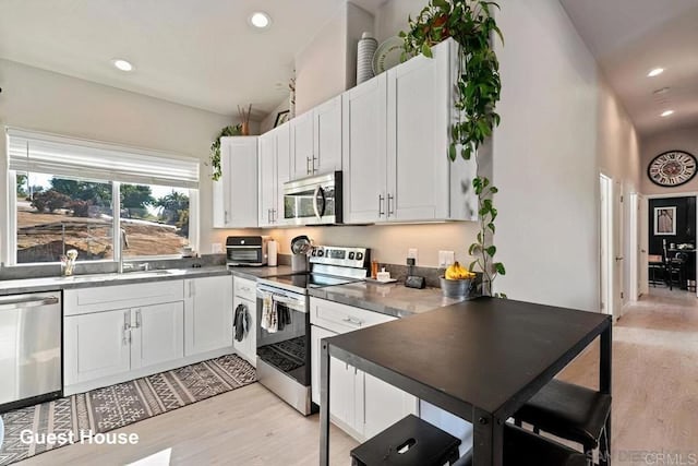 kitchen featuring light wood finished floors, appliances with stainless steel finishes, white cabinetry, and a sink