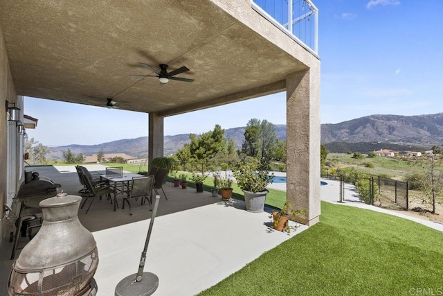 view of patio with a mountain view, outdoor dining area, a ceiling fan, and fence