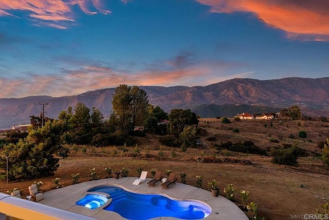 pool at dusk with a mountain view, a patio, and a pool with connected hot tub