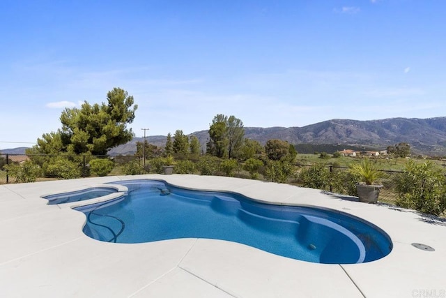 view of swimming pool with a patio area, a mountain view, a pool with connected hot tub, and fence