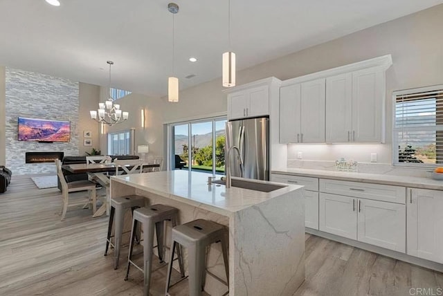 kitchen with light wood-type flooring, white cabinetry, freestanding refrigerator, a large fireplace, and light stone countertops