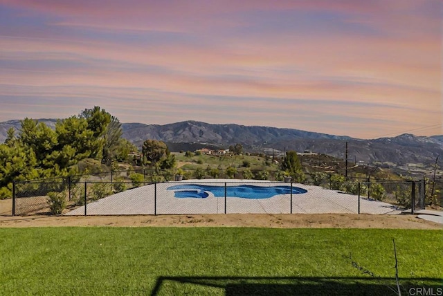 pool at dusk featuring a yard, fence, and a mountain view