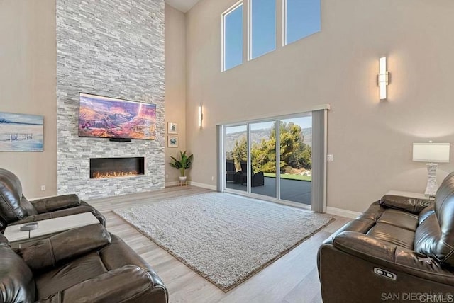 living room featuring a stone fireplace, baseboards, and wood finished floors