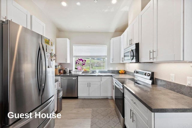 kitchen with dark countertops, recessed lighting, white cabinets, stainless steel appliances, and a sink