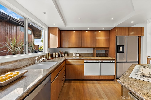 kitchen with a sink, a tray ceiling, brown cabinets, and appliances with stainless steel finishes