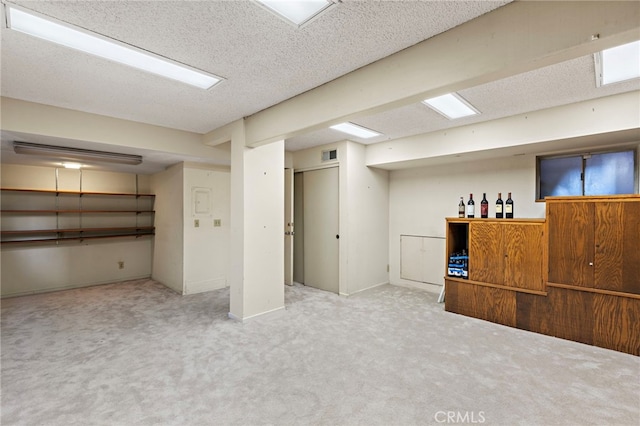 finished basement featuring visible vents, a textured ceiling, and carpet floors