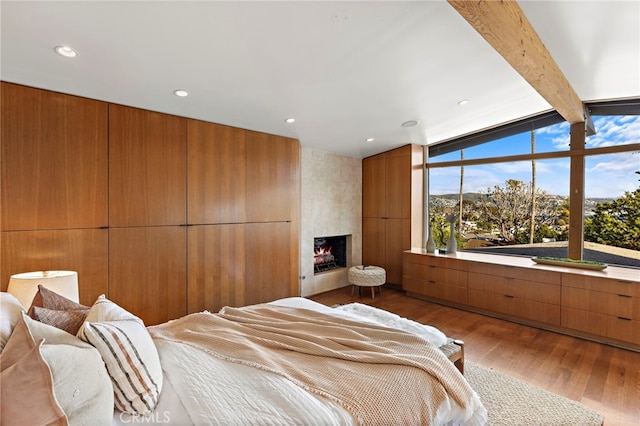 bedroom with lofted ceiling with beams, recessed lighting, wood finished floors, and a large fireplace