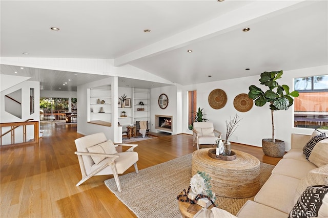 living area with lofted ceiling with beams, a warm lit fireplace, wood finished floors, and recessed lighting