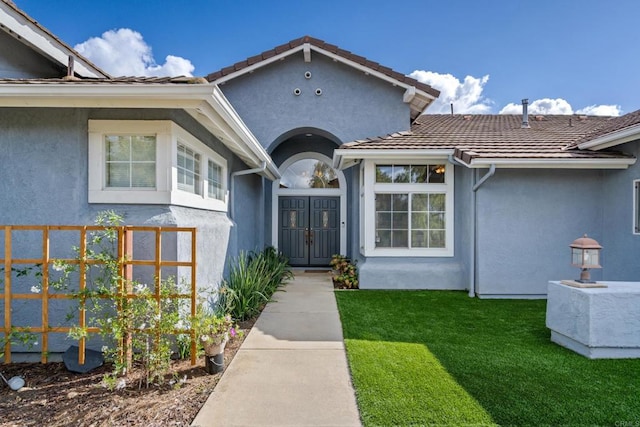 doorway to property with stucco siding, fence, a lawn, and a tile roof