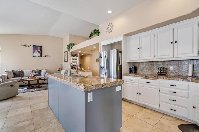 kitchen with lofted ceiling, a sink, stainless steel fridge, white cabinets, and open floor plan