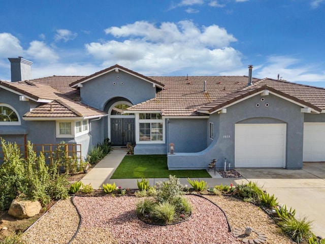 mediterranean / spanish-style house featuring driveway, an attached garage, a chimney, stucco siding, and a tile roof