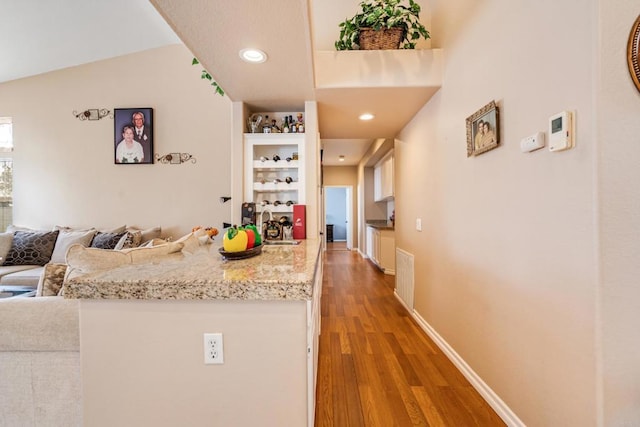 kitchen featuring light stone countertops, baseboards, light wood finished floors, a sink, and open floor plan