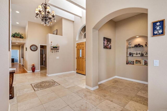 tiled foyer with a notable chandelier, baseboards, arched walkways, and a towering ceiling