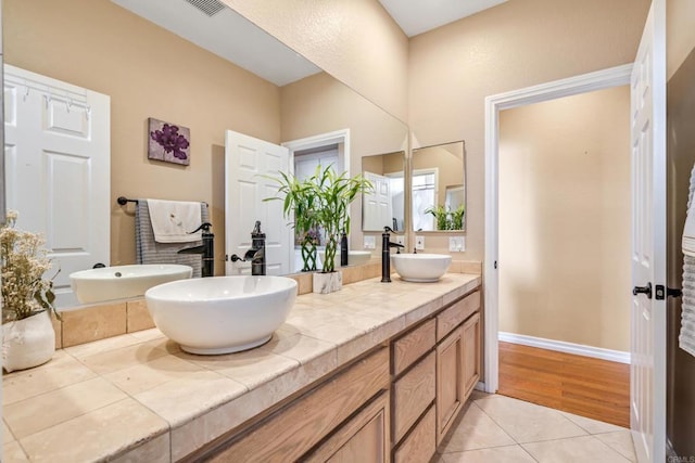 full bath featuring double vanity, tile patterned flooring, baseboards, and a sink