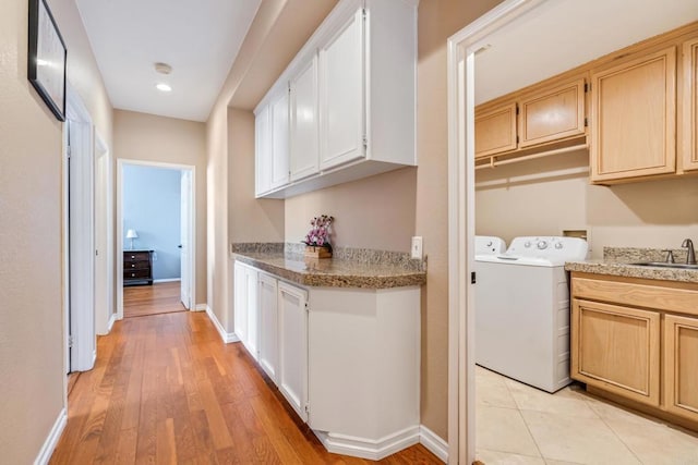 clothes washing area with light wood-style flooring, washer and clothes dryer, a sink, baseboards, and laundry area