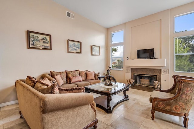 living area featuring light tile patterned floors, baseboards, visible vents, a fireplace with flush hearth, and vaulted ceiling