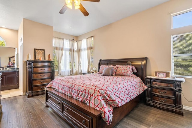 bedroom featuring connected bathroom, dark wood-style floors, baseboards, and ceiling fan