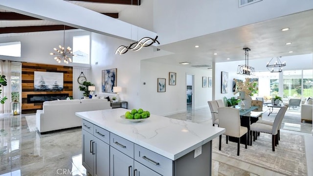 kitchen with beam ceiling, gray cabinetry, open floor plan, an inviting chandelier, and hanging light fixtures