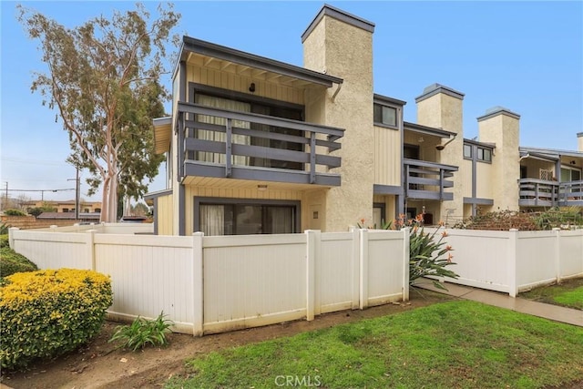 rear view of property featuring a fenced front yard, stucco siding, a chimney, and a balcony