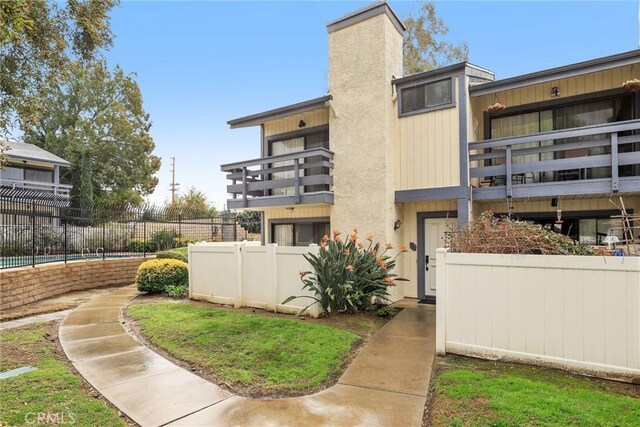 rear view of property with a balcony, a chimney, and fence