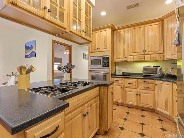 kitchen featuring visible vents, light brown cabinetry, dark countertops, stainless steel appliances, and a toaster