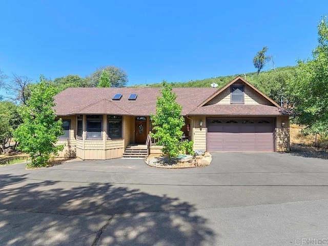 ranch-style home featuring aphalt driveway, an attached garage, and a shingled roof