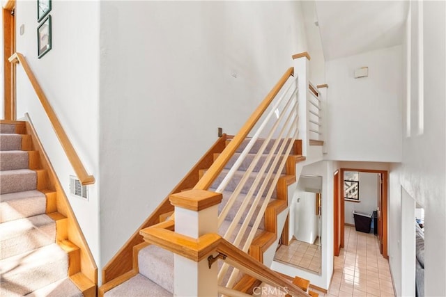 staircase with tile patterned floors, visible vents, and a high ceiling