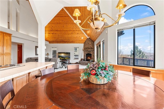 dining area featuring a stone fireplace, wooden ceiling, high vaulted ceiling, and an inviting chandelier