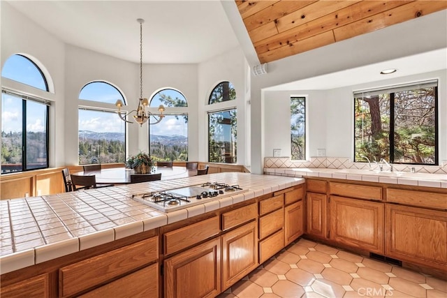 kitchen featuring tile countertops, white gas cooktop, brown cabinets, and a sink