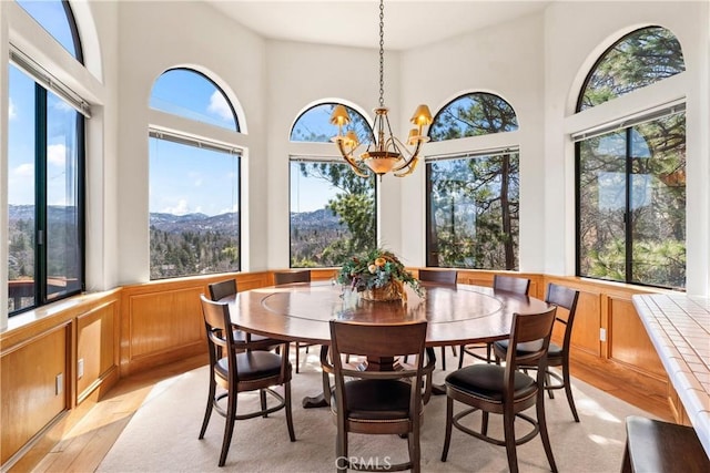 dining area with light wood-style flooring, wainscoting, a towering ceiling, and a chandelier