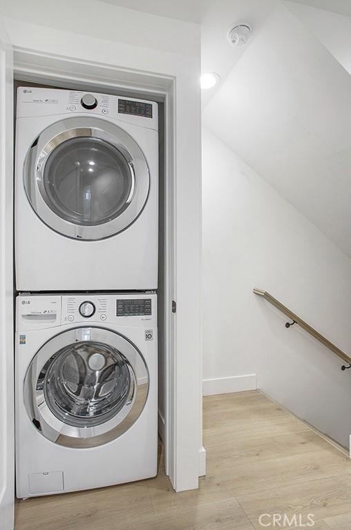 clothes washing area with wood finished floors, laundry area, and stacked washer / dryer