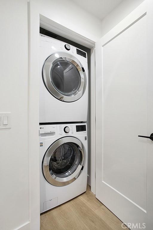 laundry room with laundry area, stacked washer / dryer, and light wood-style floors